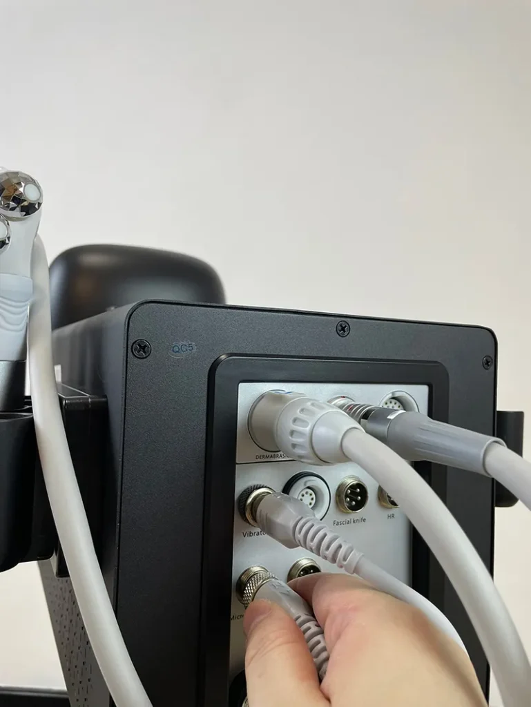 Main insérant le connecteur de la poignée microcourant à rouleau sur la prise arrière de l'appareil hydro dermabrasion, étape de branchement accessoire anti-âge pour institut de beauté