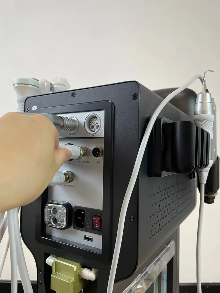 Main branchant le connecteur de la poignée nettoyeur ultrasonique pour peau (skin scrubber) sur la prise arrière de l'appareil hydro dermabrasion, étape de raccordement accessoire exfoliant visage professionnel