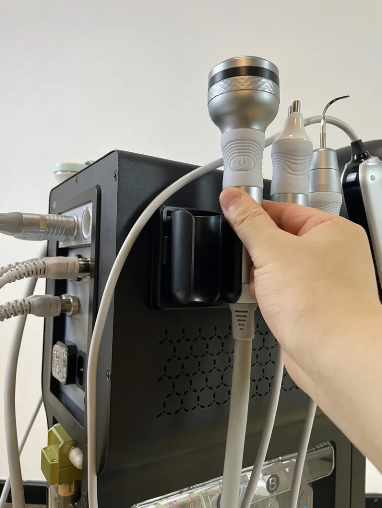 Main posant la poignée chaud-froid sur le support latéral de l'appareil hydro dermabrasion, étape d'installation accessoire thermique pour soin apaisant visage en institut