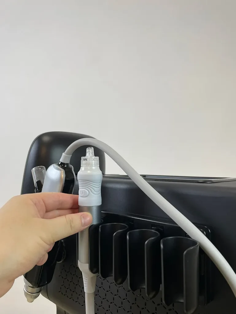 Main posant la poignée hydro dermabrasion sur son support latéral de l'appareil hydro dermabrasion, étape d'installation accessoire de peeling hydrafacial pour institut de beauté