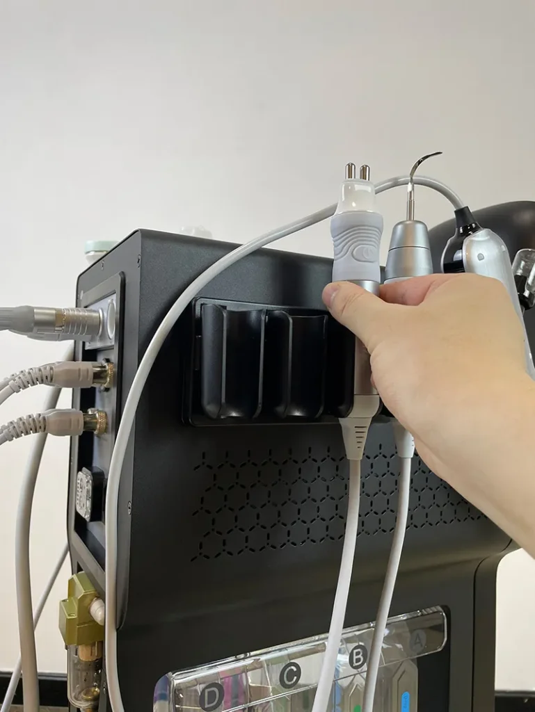 Main posant la poignée radiofréquence sur le support latéral de l'appareil hydro dermabrasion, étape d'installation accessoire lifting anti-âge pour institut de beauté