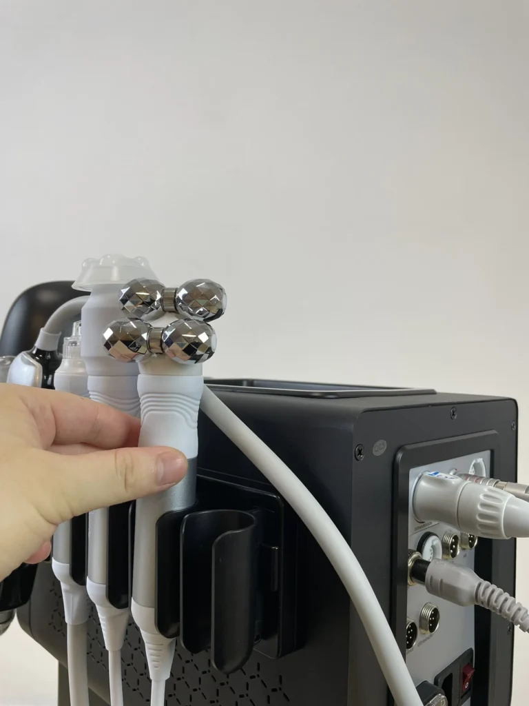 Hand placing roller microcurrent handpiece on bracket of 10 in 1 hydradermabrasion machine, anti-aging facial handle assembly step for salon skincare equipment