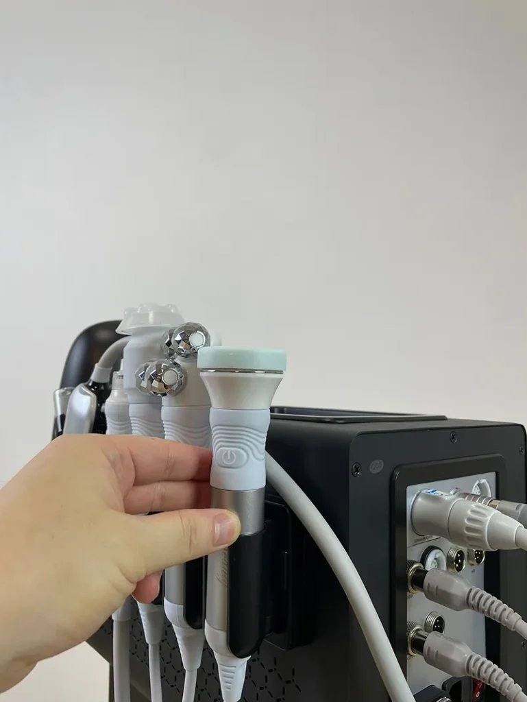 Hand placing ultrasonic handpiece onto bracket of 10 in 1 hydradermabrasion machine, deep cleansing facial handle assembly tutorial for spa beauty equipment