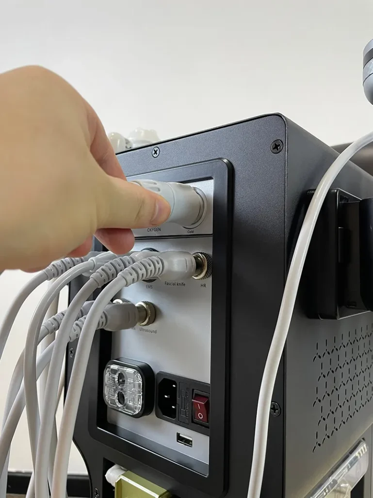 Hand plugging signal connector of cold and hot hammer handpiece into rear port of 10 in 1 hydradermabrasion machine, wiring connection installation step for skin soothing facial spa equipment