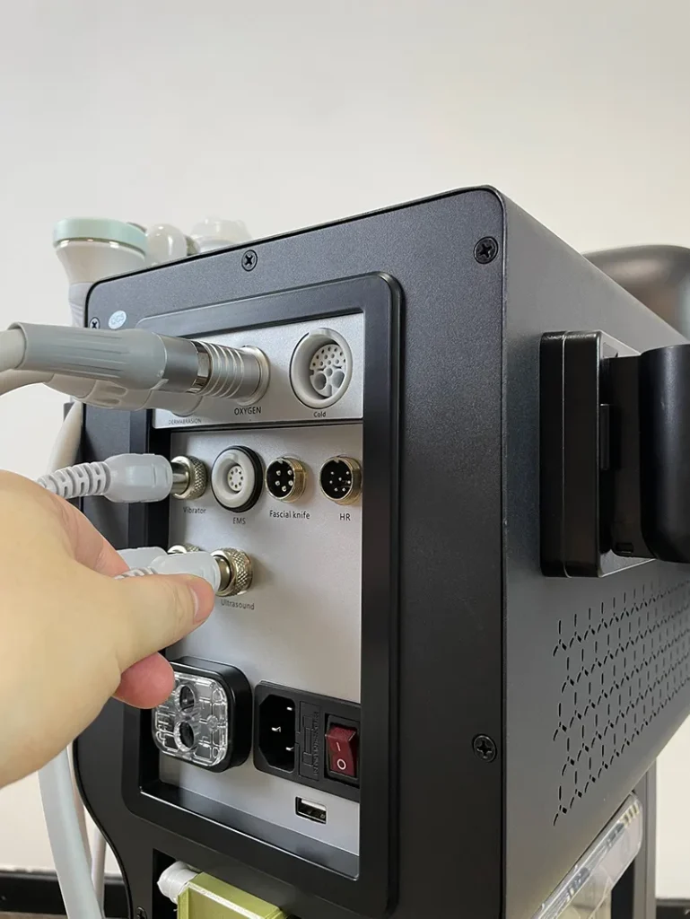Hand plugging the connector of ultrasonic handpiece into rear port of 10 in 1 hydradermabrasion machine, wiring connection installation step for facial spa equipment