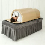 foldable infrared sauna dome placed on beauty massage bed, model lying inside receiving full body far infrared spa therapy