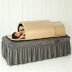 Model lying on her side inside infrared sauna dome placed on salon massage bed for far infrared wellness therapy